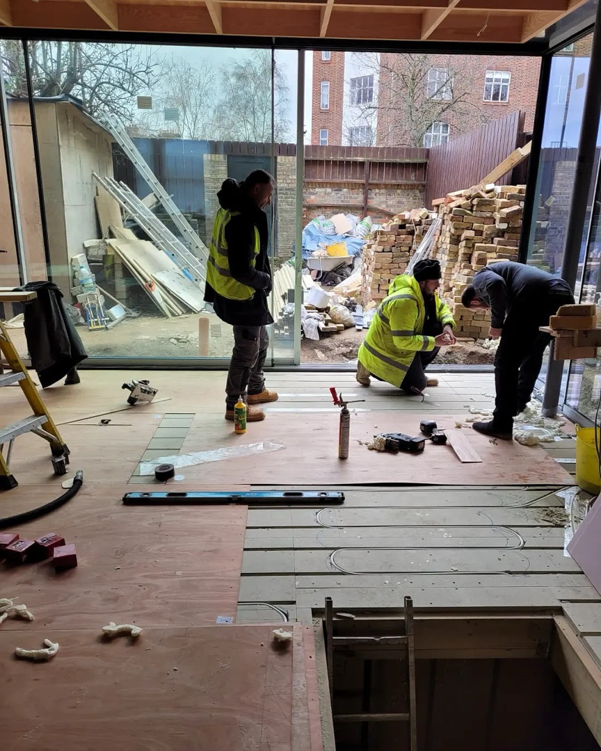 Three builders laying the new floor beside large glass doors at the back of a house